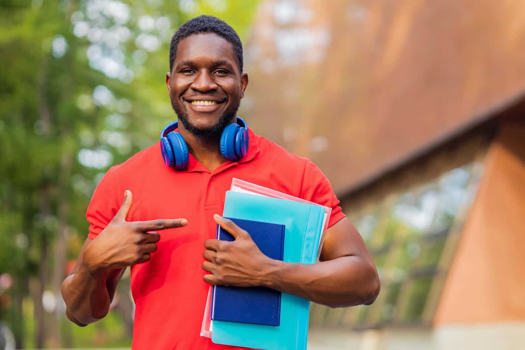 young-afro-american-man-with-headphones-neck-holding-book-folder-hands-summer-park